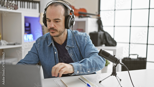 Hispanic man with beard working in indoor music studio wearing headphones and denim jacket