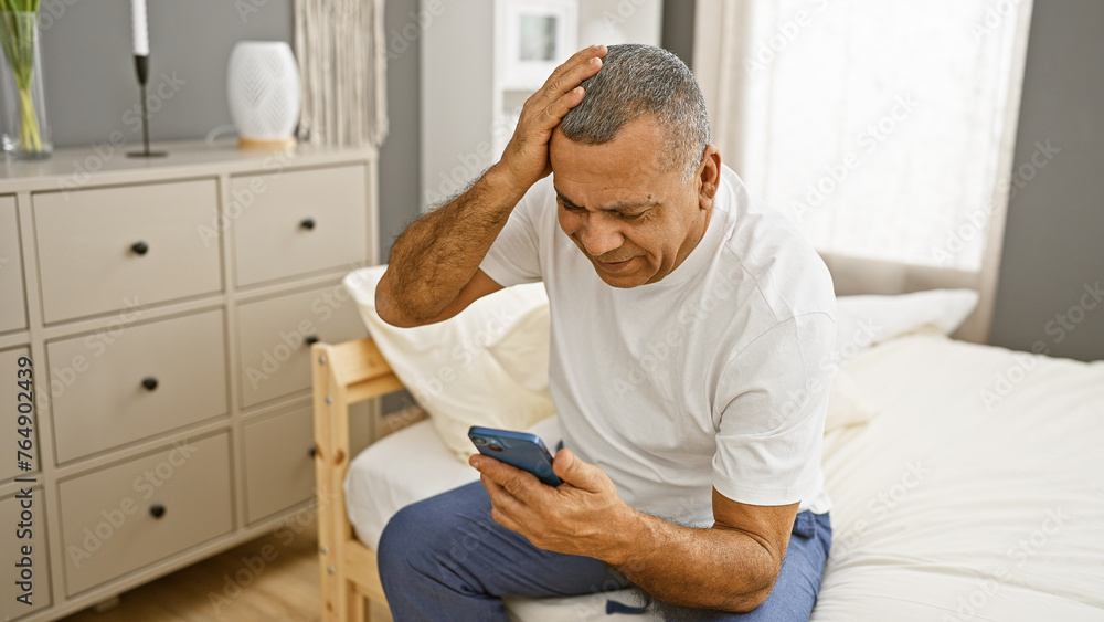 Worried middle-aged hispanic man using smartphone in bedroom interior setting. Worried middle-aged hispanic man using smartphone in bedroom interior setting.