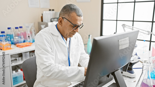 Middle-aged hispanic man in lab coat analyzing data on computer in a bright laboratory setting