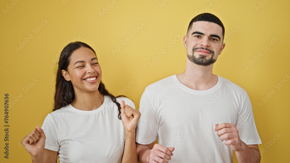 Confident, beautiful couple together, smiling and dancing. standing against isolated yellow background, expressing joy and love Confident, beautiful couple together, smiling and dancing. standing against isolated yellow background, expressing joy and love