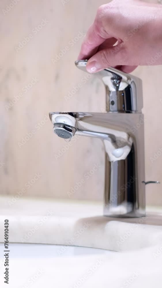 Close-up slow motion of caucasian female hand opening a mixer tap in a hotel bathroom. Beautiful fresh and clean water running from a shiny chrome faucet into a washbasin. Wasting water and energy. Close-up slow motion of caucasian female hand opening a mixer tap in a hotel bathroom. Beautiful fresh and clean water running from a shiny chrome faucet into a washbasin. Wasting water and energy.