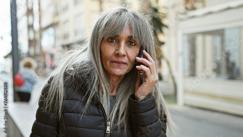 A mature woman with grey hair talks on a phone on a city street, portraying a moment of urban life.