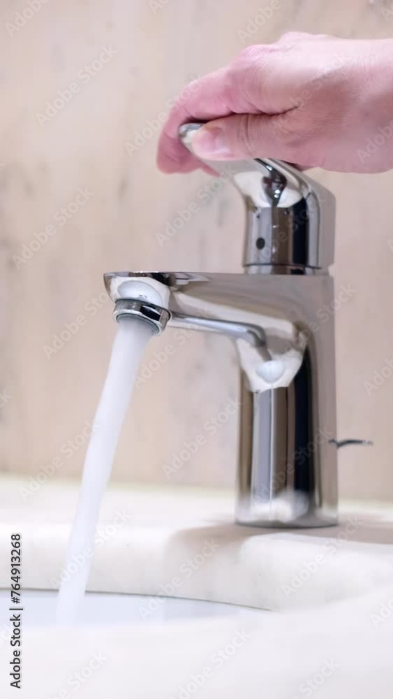 Close-up slow motion of caucasian female hand opening a mixer tap in a hotel bathroom. Beautiful fresh and clean water running from a shiny chrome faucet into a washbasin. Wasting water and energy. Close-up slow motion of caucasian female hand opening a mixer tap in a hotel bathroom. Beautiful fresh and clean water running from a shiny chrome faucet into a washbasin. Wasting water and energy.