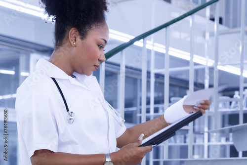 young african american woman doctor reading medical research from clipboard in lab at hospital. female doctor student studying medical report in laboratory in university. medical education.