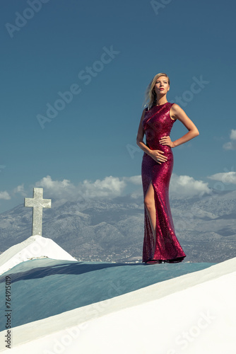 Beautiful young woman in elegant red dress posing on the roof. Fashion concept. © Paopano