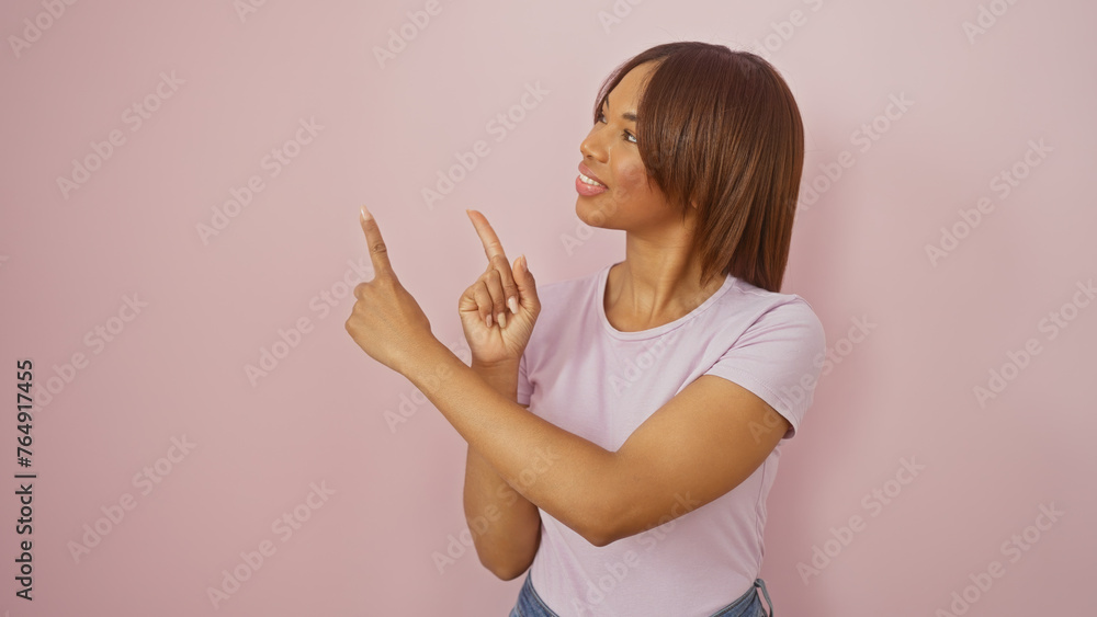 Attractive black woman pointing sideways against a pink isolated background, displaying confidence and style. Attractive black woman pointing sideways against a pink isolated background, displaying confidence and style.