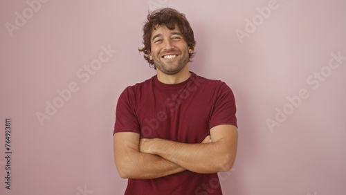 Handsome hispanic man with a beard smiling with arms crossed against a pink wall in a casual maroon shirt. © Krakenimages.com