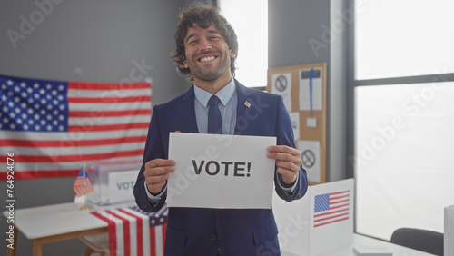 A young hispanic man with a beard holding a 'vote!' sign in a room with american flags © Krakenimages.com