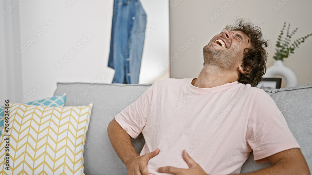 Laughing young hispanic man relaxing comfortably indoors in a modern apartment living room setting. Laughing young hispanic man relaxing comfortably indoors in a modern apartment living room setting.