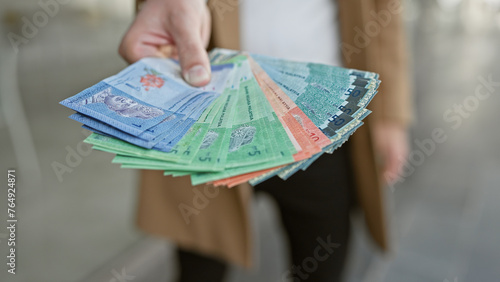 Man holding malaysian ringgit banknotes on an urban street.