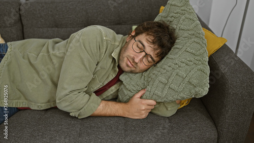 Foto A young man with glasses sleeps cozily with a green pillow on a gray couch at home