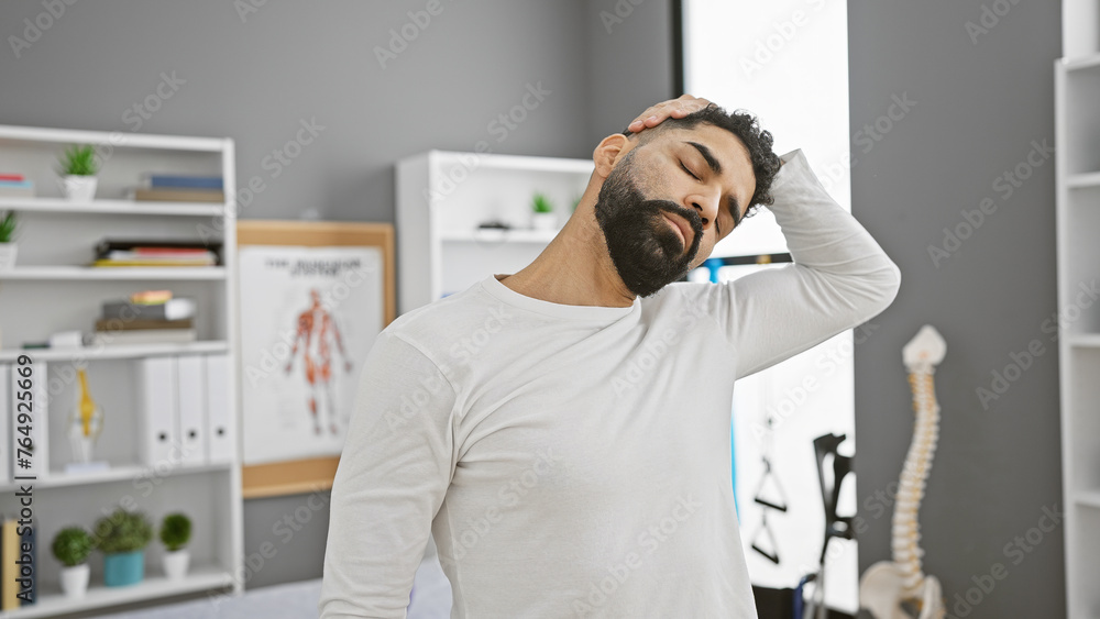 Fototapeta premium A young hispanic man with a beard in neck pain at a modern rehabilitation clinic.