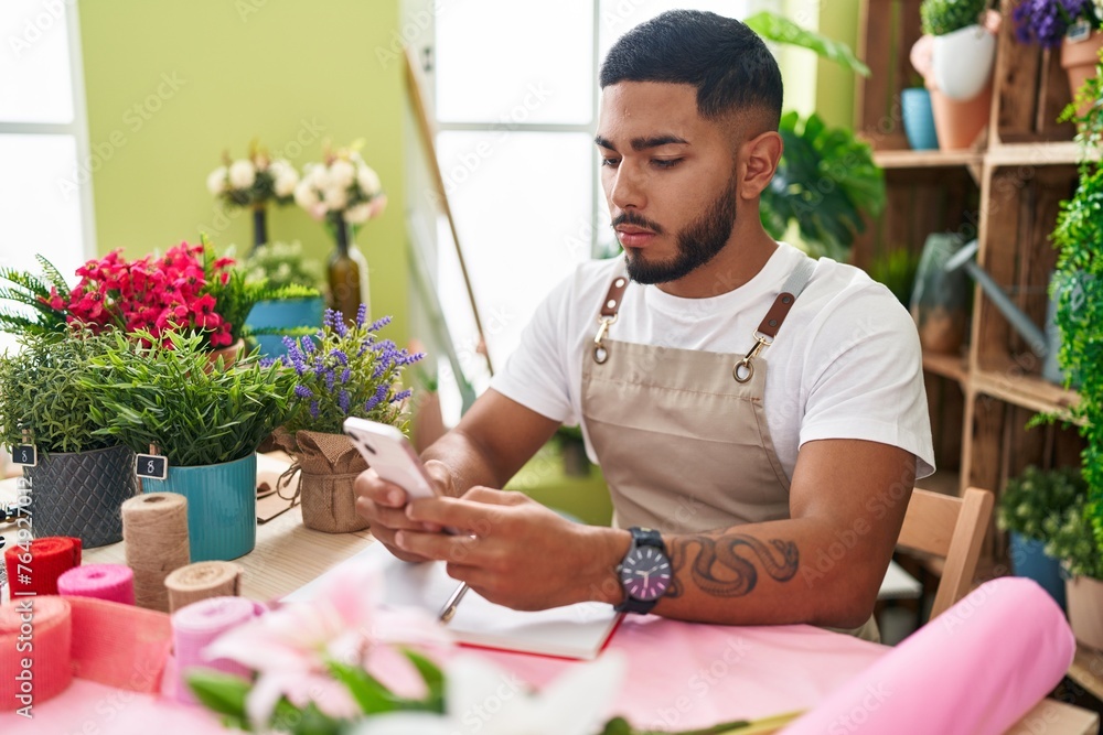 Young latin man florist using smartphone at flower shop