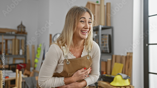 Caucasian mature woman with blonde hair smiling in a workshop with safety helmet and wooden materials in the background