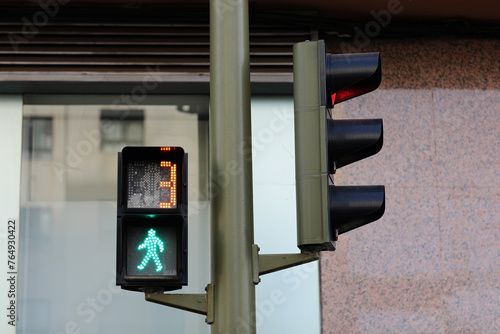 Pedestrian traffic light with green permissive signal and countdown, little green walking man, number 3, building background. Traffic lights regulate the movement of pedestrians across the roadway. photo