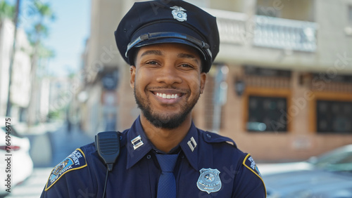A smiling african american police officer stands confidently outdoors on a city street.