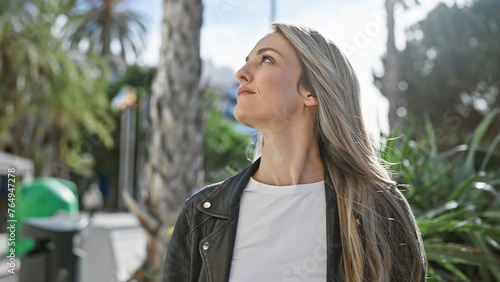 Valokuva A contemplative young blonde woman outdoors in city surroundings, looking upward with a hopeful expression
