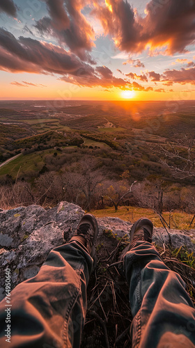 A hiker's view from the top of a hill, overlooking a vast valley, colorful sunset in the background, feeling of accomplishment and awe