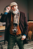 Portrait d'un photographe créatif et original de type hispter très élégant et stylé avec un manteau un béret et un gilet dans un atelier créatif