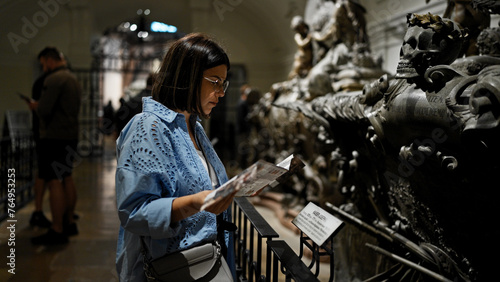 Young beautiful hispanic woman visiting crypt reading brochure at Imperial Crypt in Vienna