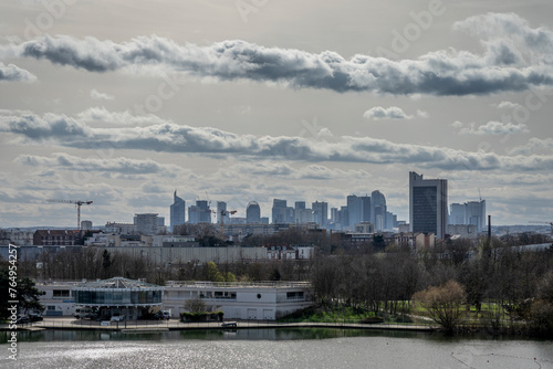 Gennevilliers, France - 03 16 2024: Chanteraines park. Nature in bloom in spring season. View of the artificial pond and the towers of La Defense district behind.