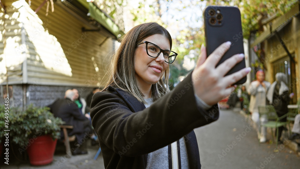 A young brunette woman takes a selfie on an urban istanbul street, showcasing travel and city life. A young brunette woman takes a selfie on an urban istanbul street, showcasing travel and city life.