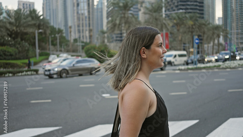 A young brunette woman wearing casual clothing stands by a crosswalk amidst the modern skyscrapers of dubai's cityscape. © Krakenimages.com