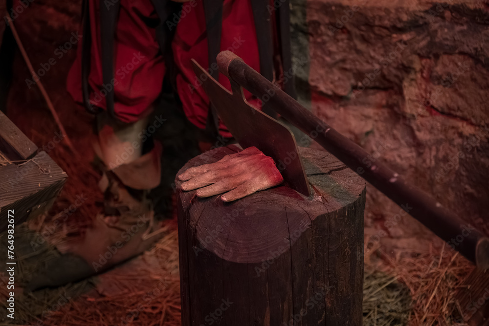 A severed hand by the executioner's ax on a log in the torture chamber. - obrazy, fototapety, plakaty 