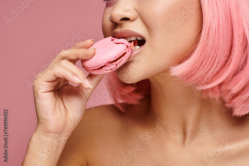 cropped shot of young woman with pink hair eating macaroon against vibrant background