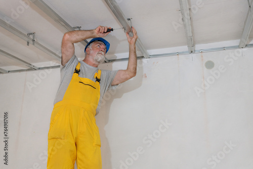 Worker placing aluminum profile for gypsum ceiling and insulation using screwdriver