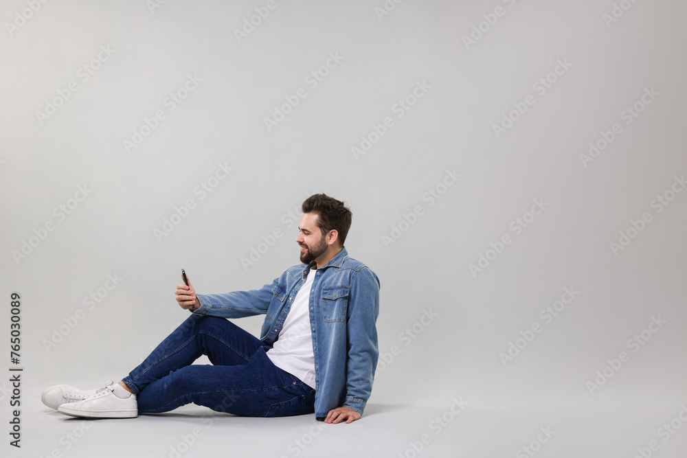 Handsome young man using smartphone on grey background, space for text Handsome young man using smartphone on grey background, space for text
