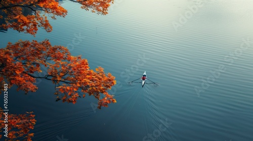 Person rowing on a calm lake in autumn, aerial view only small boat 
