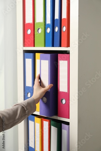 Woman taking binder office folder from shelving unit indoors, closeup