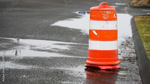A vivid orange and white traffic cone stands out against the dark, wet asphalt of a road