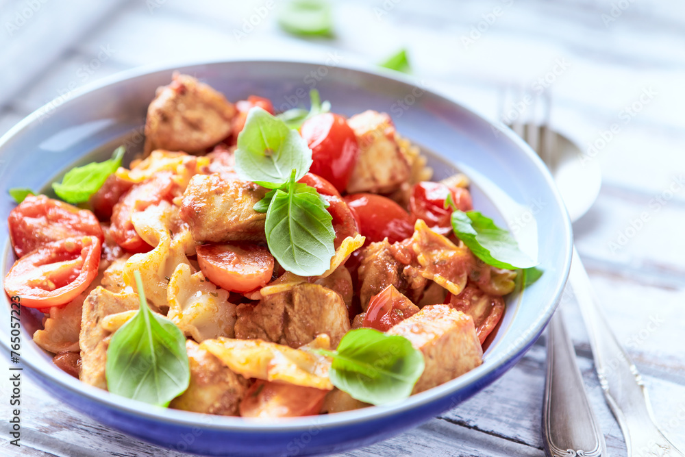 Farfalle pasta with chicken breast, cherry tomatoes and fresh basil. Bright wooden background. Close up.	