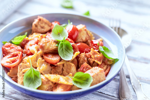 Farfalle pasta with chicken breast, cherry tomatoes and fresh basil. Bright wooden background. Close up. 