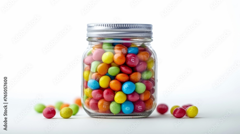 Brightly colored candies fill a transparent glass jar, with a few scattered around, against a stark white background. Brightly colored candies fill a transparent glass jar, with a few scattered around, against a stark white background.