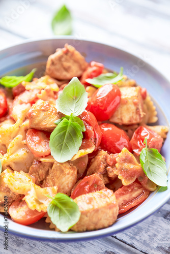 Farfalle pasta with chicken breast, cherry tomatoes and fresh basil. Bright wooden background. Close up.	
