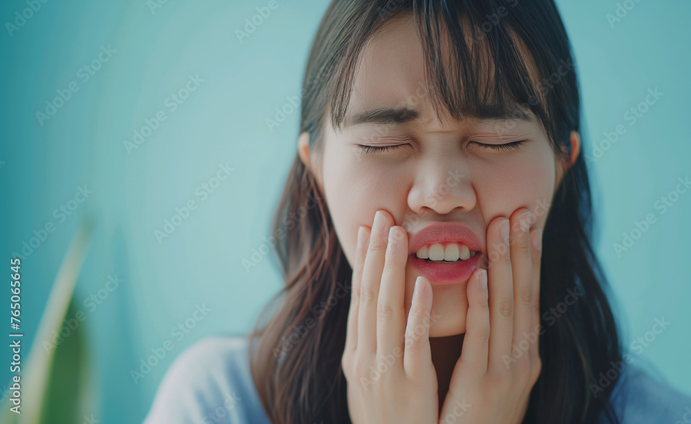 A woman expressing pain by holding her cheeks and closing her eyes, indicating a possible toothache or facial discomfort. A woman expressing pain by holding her cheeks and closing her eyes, indicating a possible toothache or facial discomfort.