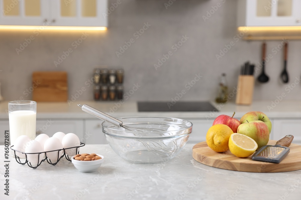 Metal whisk, bowl, grater and different products on gray marble table in kitchen Metal whisk, bowl, grater and different products on gray marble table in kitchen
