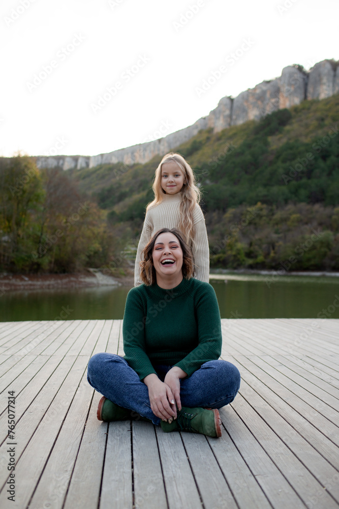 A happy mom  and daoghter have fun  against the background of a lake, forest and mountain. People breathes fresh healthy air. Outdoor weekend concept