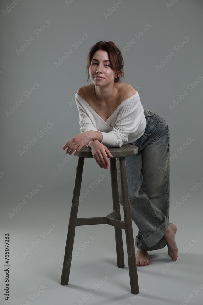 Beautiful young woman posing near stool on grey background Beautiful young woman posing near stool on grey background