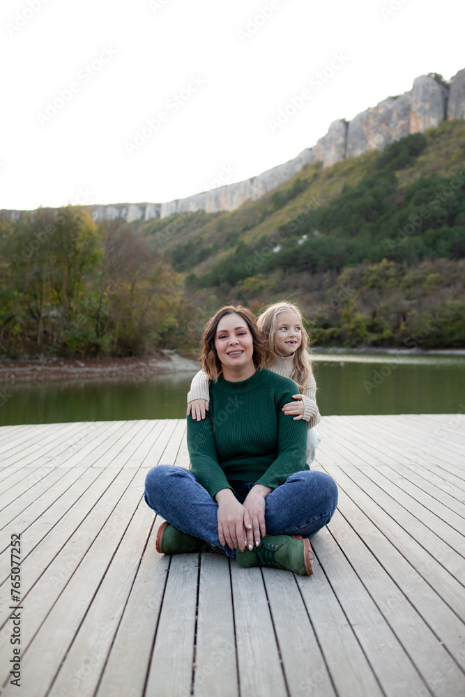 A happy mom  and daoghter have fun  against the background of a lake, forest and mountain. People breathes fresh healthy air. Outdoor weekend concept