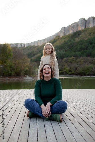 A happy mom and daoghter have fun against the background of a lake, forest and mountain. People breathes fresh healthy air. Outdoor weekend concept