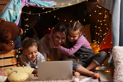 Mother and her children with laptop in play tent at home