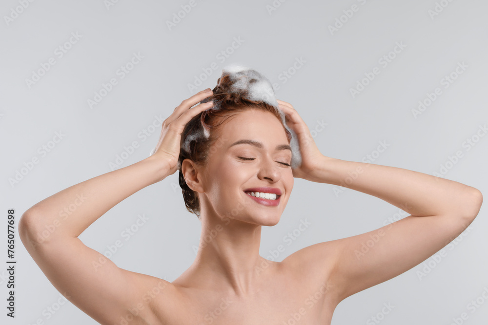 Happy young woman washing her hair with shampoo on light grey background Happy young woman washing her hair with shampoo on light grey background
