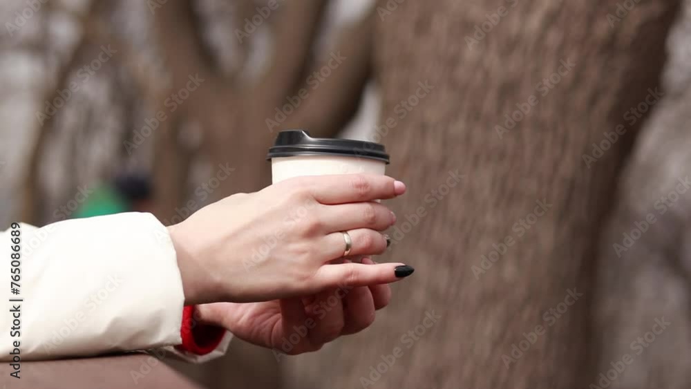 A disposable cardboard cup with tea or coffee in female hands close-up. Takeaway coffee. A girl holds a paper cup with a hot drink in the park, autumn or spring, cool weather A disposable cardboard cup with tea or coffee in female hands close-up. Takeaway coffee. A girl holds a paper cup with a hot drink in the park, autumn or spring, cool weather