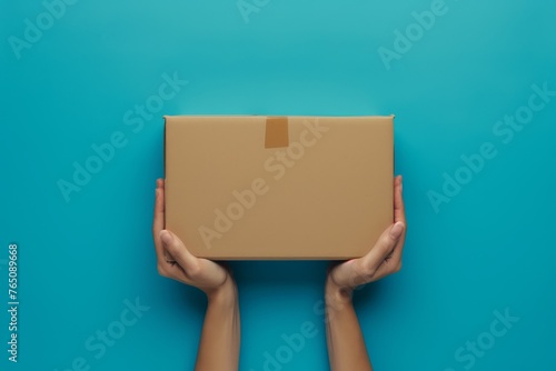 top view The person is holding a cardboard box with a fashion accessory inside. The background is electric blue, resembling a skyscraper. The box is a rectangle shape, held delicately by their wrist photo