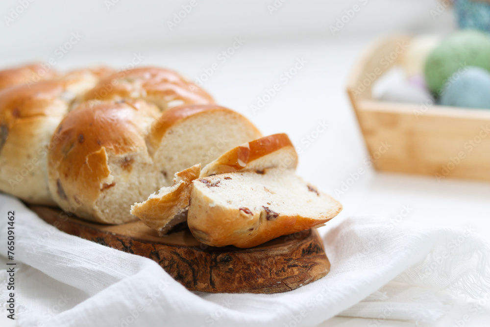 Cutted easter loaf bread on wooden plate on white table, blurry background with easter decoration Cutted easter loaf bread on wooden plate on white table, blurry background with easter decoration