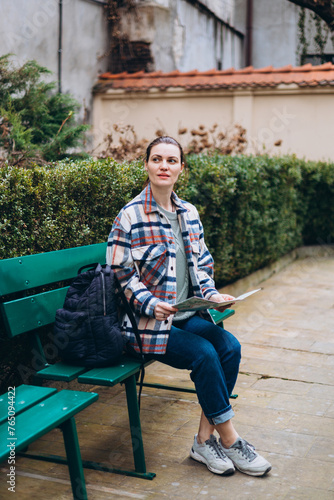 Beautiful stylish 30s woman in trendy wear spending time on street using paper map. Happy girl sitting on the bench. Urban lifestyle concept, travel banner